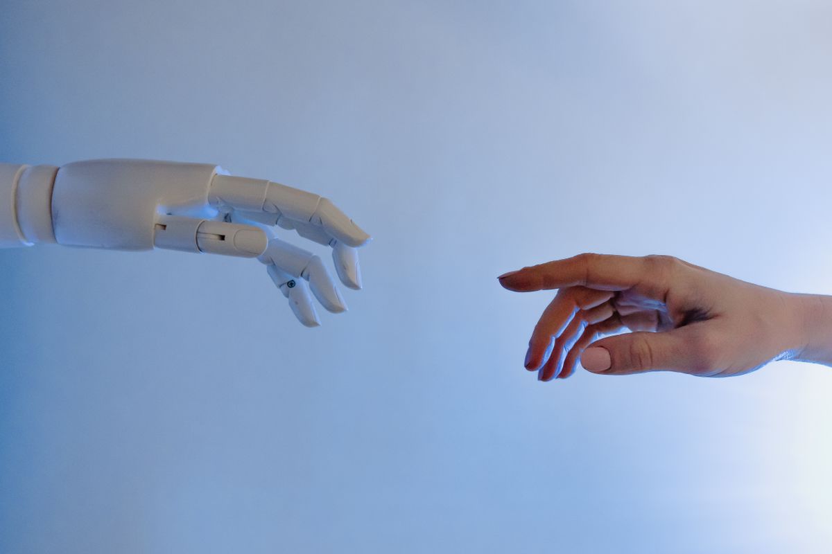 A robotic hand and a human hand reaching toward each other, not quite touching